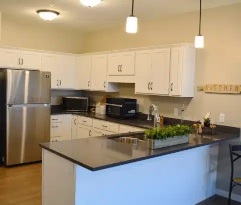 Bright modern kitchen with white cabinets, a stainless steel fridge, and a gray island with a sink and pendant lights above it.