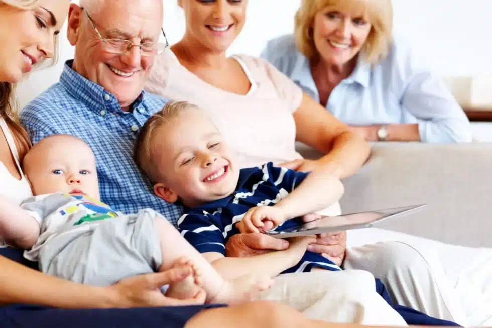 Smiling multi-generational family sitting on a sofa, looking at a tablet together.
